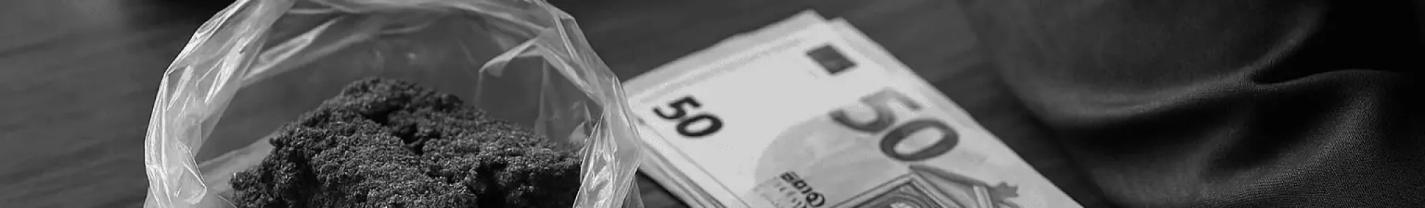 Un hombre apoyado en una mesa con estupefacientes y dinero